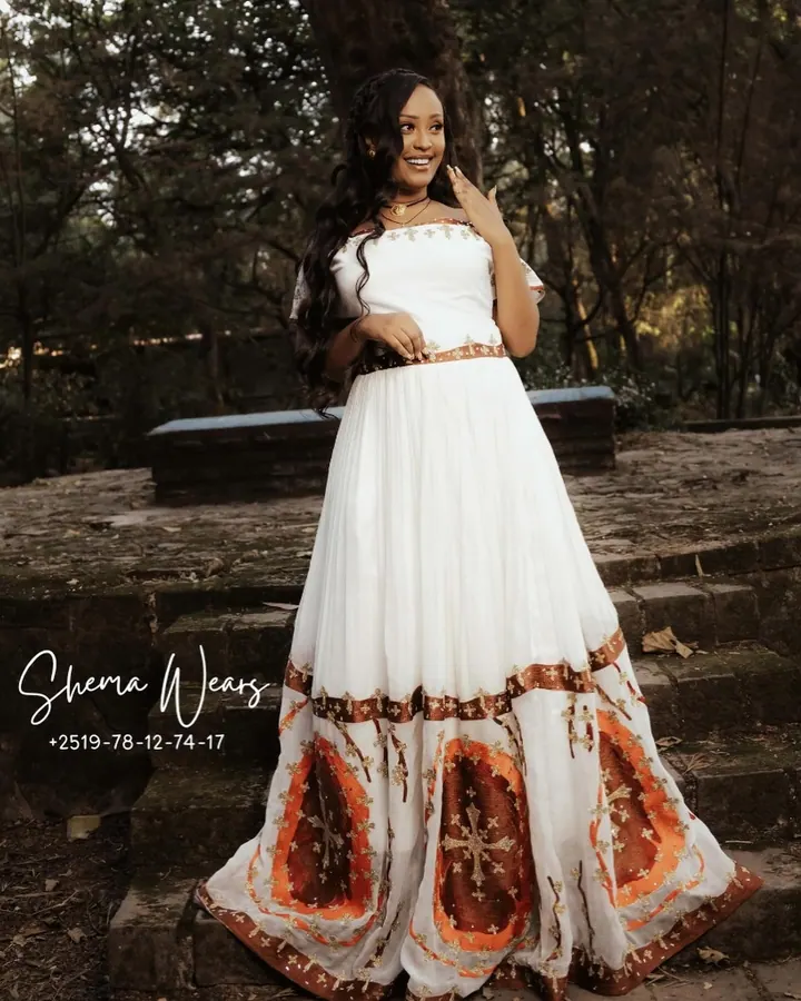 Model in a white habesha kemis with short sleeves, a brown belt and large amber and orange medallions around the skirt