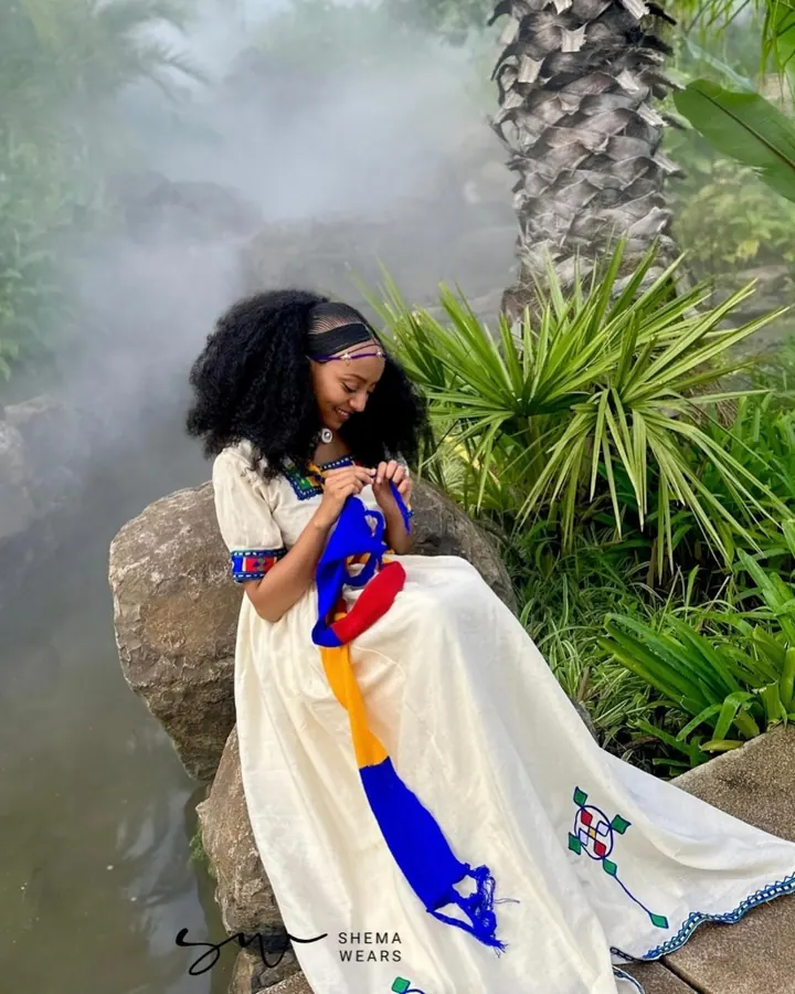 Woman in a white habesha dress with colourful ribbon sashes and small embroidered crosses, for Ashenda