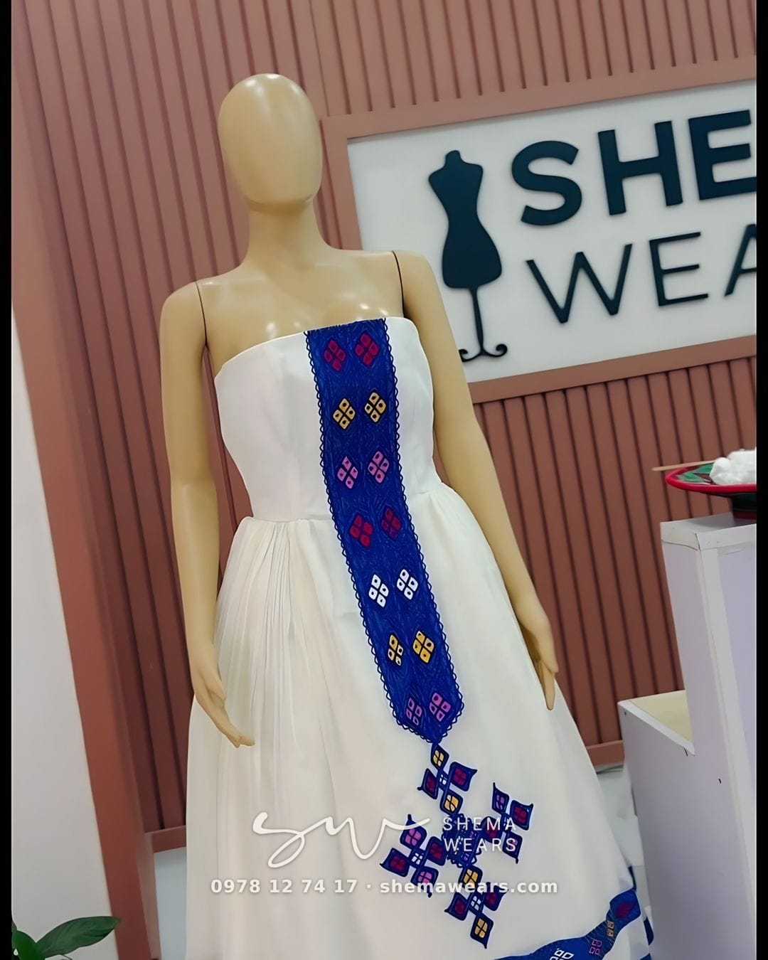 ኣብ ማኒኪን ዘሎ ማንጠልጠሊ ዘይብሉ ጻዕዳ ሓበሻ ቀሚሽ፣ ሰማያዊ መስመር ጥበብ፣ ሰማያዊ መስቀልን ኣብ ጫፉ ሰማያዊ መስመራትን ዘለዎ