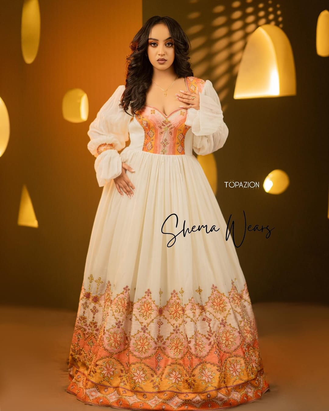 Bride in a white habesha kemis with sheer balloon sleeves, a long open overlay and coral tibeb down the front and hem