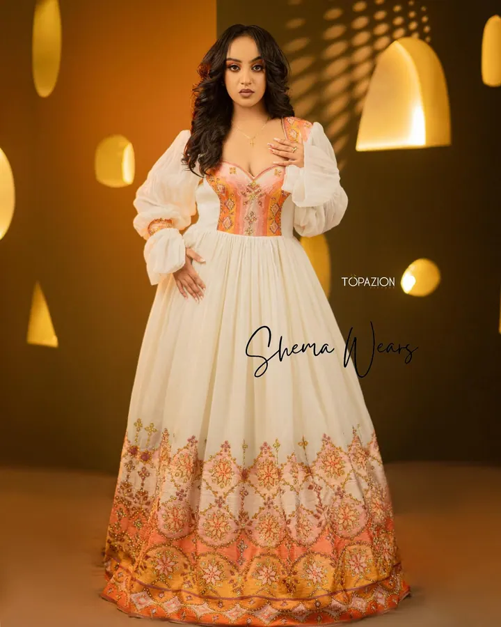 Bride in a white habesha kemis with sheer balloon sleeves, a long open overlay and coral tibeb down the front and hem
