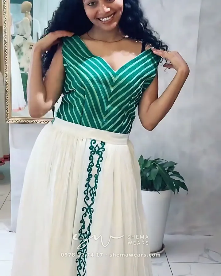 Model in a habesha kemis with an emerald and white striped bodice, green tibeb down the skirt and an emerald hem