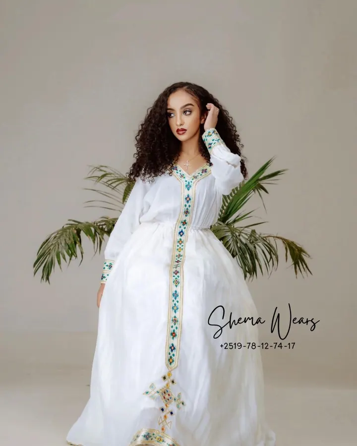 Model in a white long-sleeve habesha kemis with fine green and gold tibeb down the front and sleeves