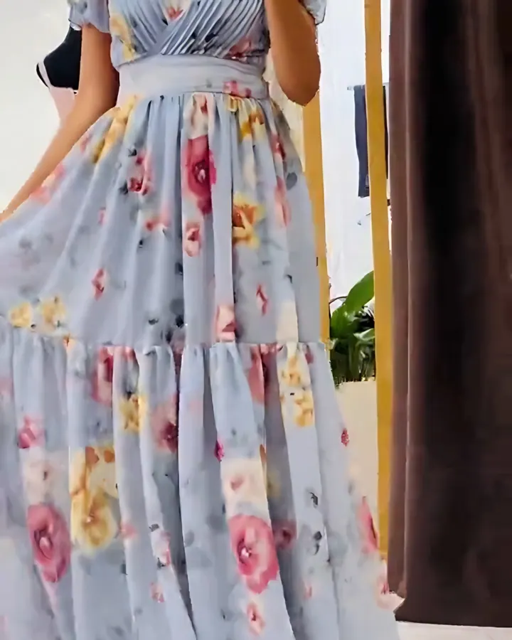 Woman in a long blue-grey chiffon dress with pink and yellow flowers, puff sleeves and a wrap neckline