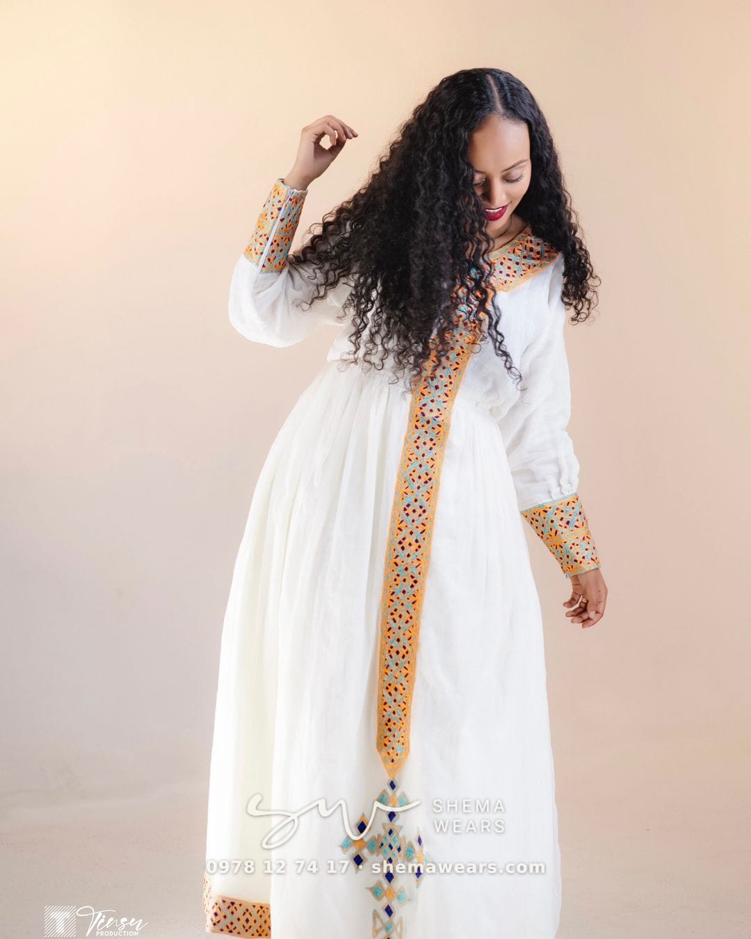Model in a white long-sleeve habesha kemis with a gold tibeb panel down the front and gold cuffs