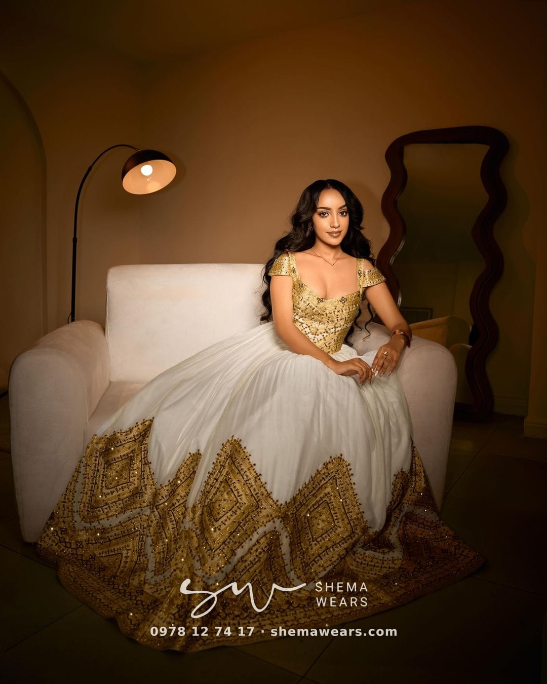 Seated model in a white ballgown habesha kemis with a gold tibeb bodice, cap sleeves and a deep hem of gold tibeb diamonds