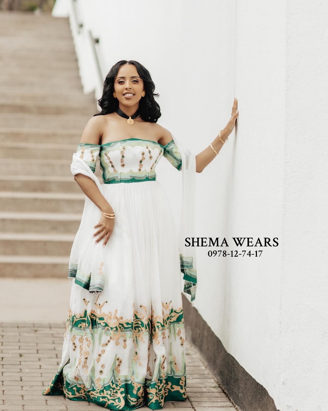 Model in a white off-shoulder habesha kemis with puff sleeves and green floral tibeb on the bodice and skirt