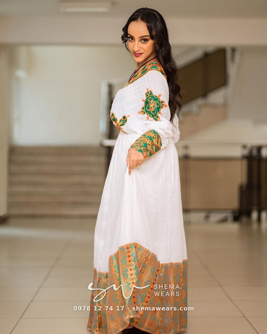 ሞዴል፣ ኣብ ነዊሕ ኢዱ ቀጠልያን ወርቃውን ጥበብን ኣብ ጫፉ ሰፊሕ ወርቃዊ ጥበብን ዘለዎ ጻዕዳ ሓበሻ ቀሚሽ ተኸዲና