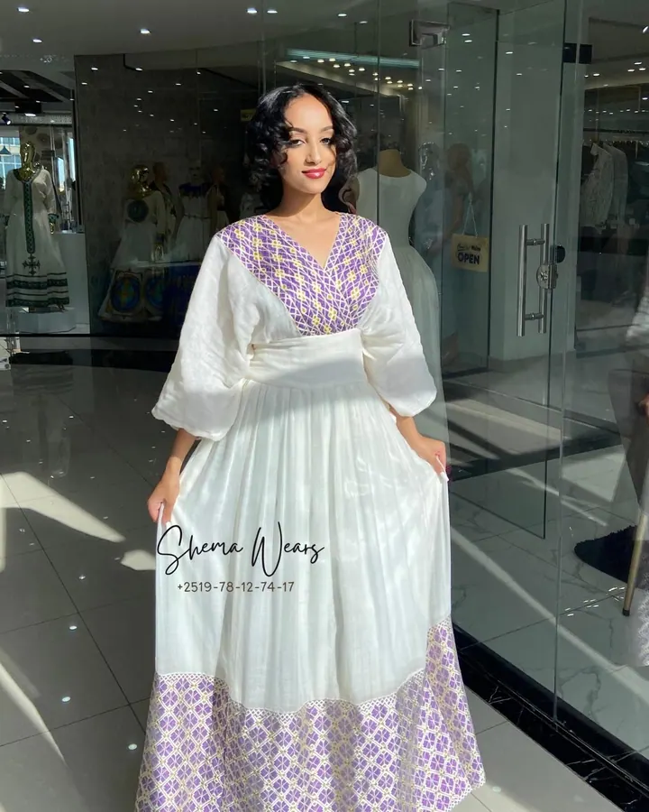 Model in a white habesha kemis with a lavender geometric tibeb bodice, puff sleeves and a wide lavender tibeb hem
