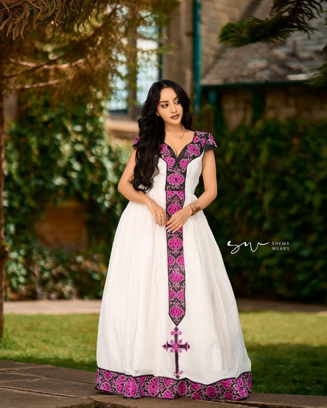 Woman in a white habesha kemis with magenta and black tibeb down the front ending in a cross