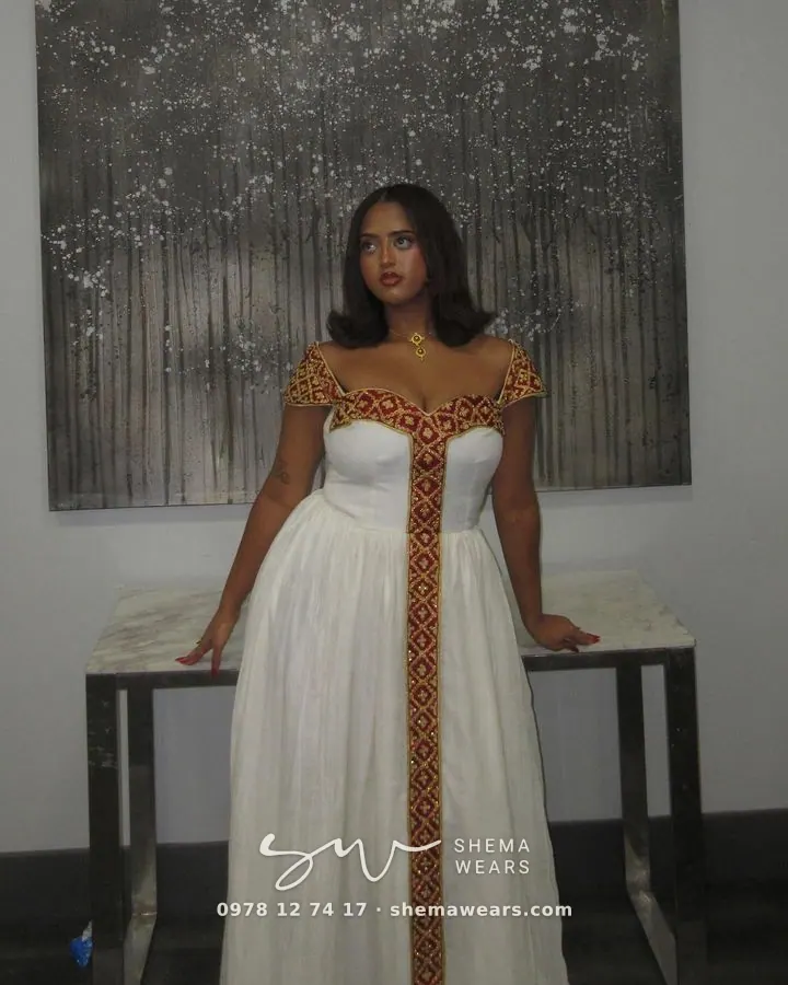 Model in a white habesha kemis with maroon and gold tibeb at the sweetheart neckline, cap sleeves and centre panel