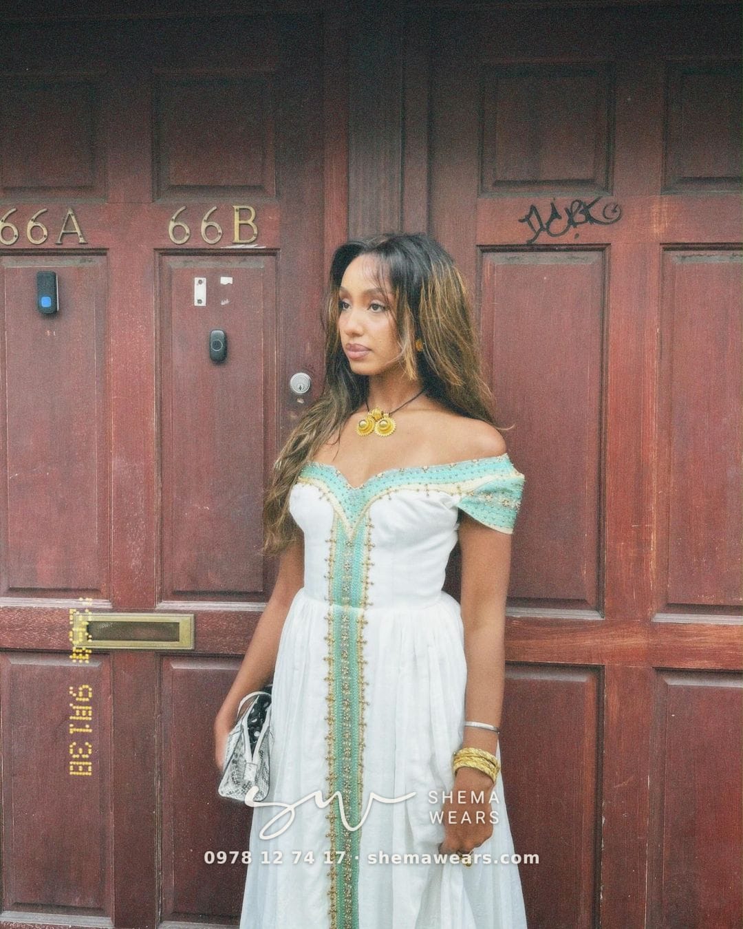 Model in a white off-shoulder habesha kemis with mint green and gold tibeb down the front