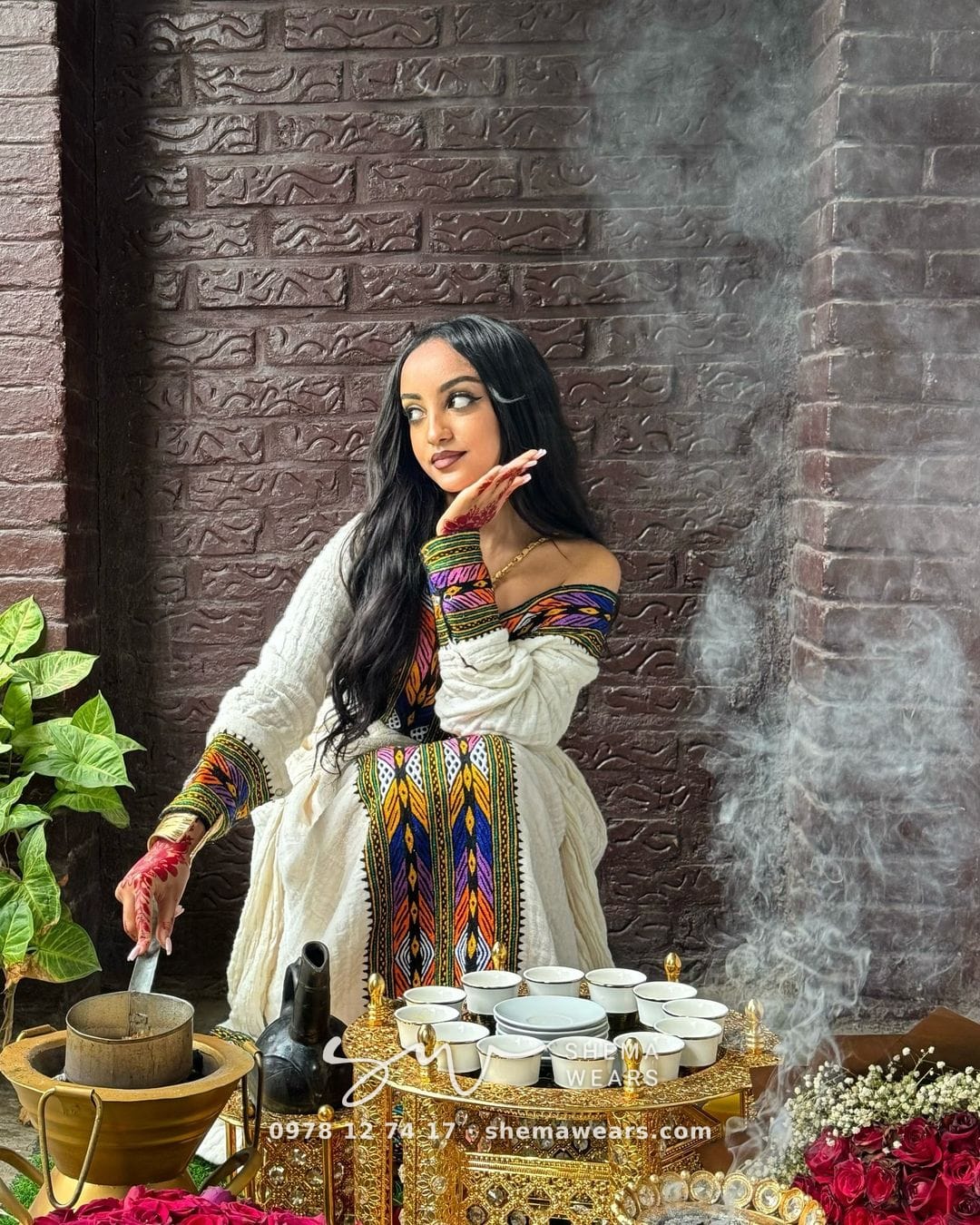 Woman at a coffee ceremony in a white off-shoulder habesha kemis with multicolour tibeb on the bodice and sleeves