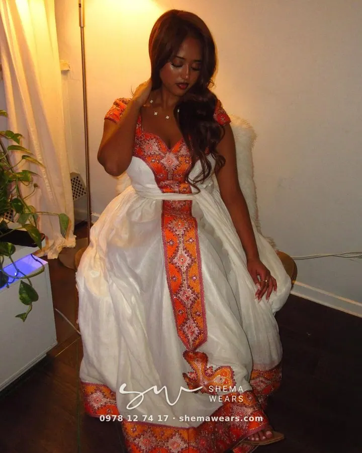 Model in a white habesha kemis with an orange and pink embroidered bodice, centre panel and a white belt