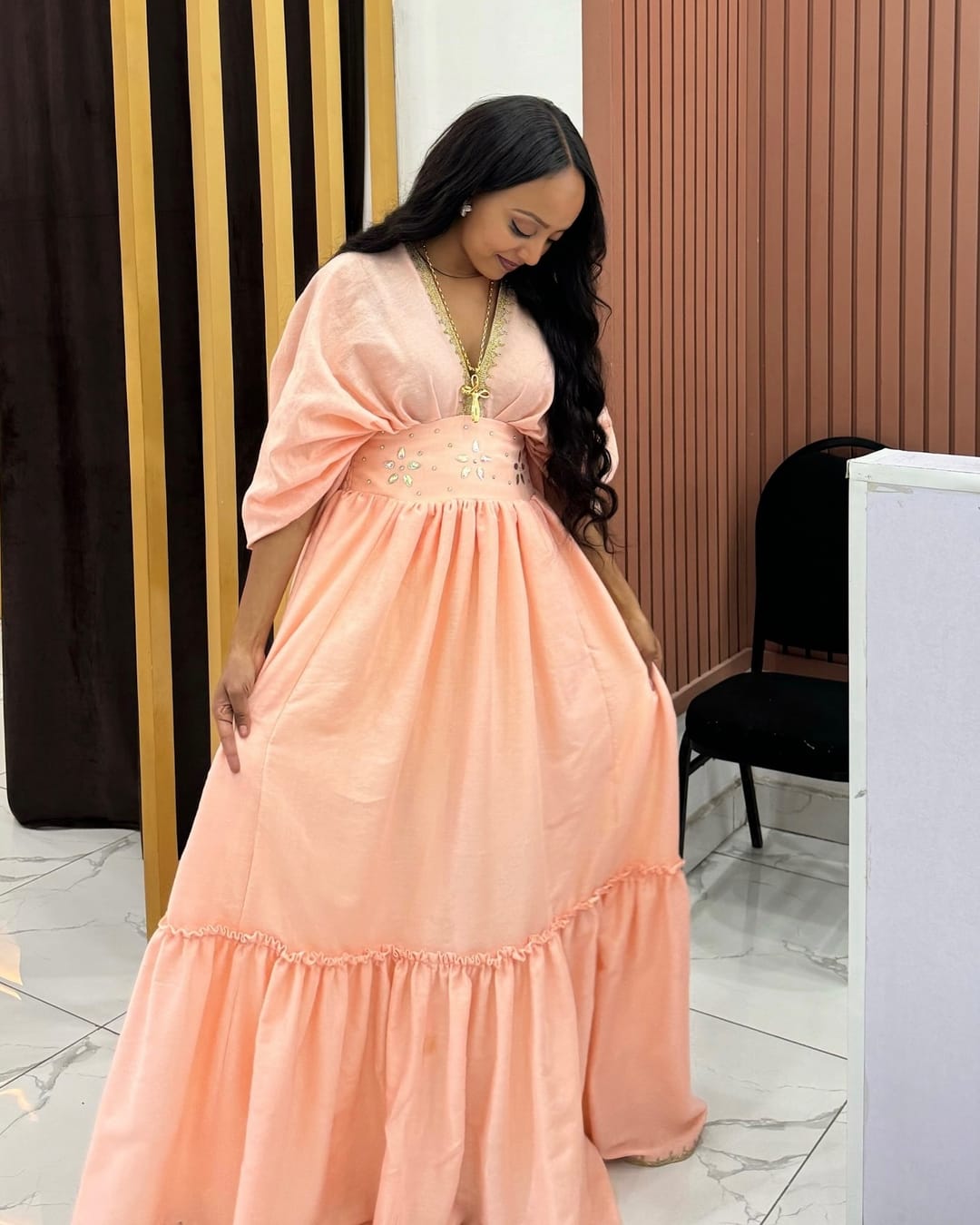 Model in a long peach chiffon dress with wide puff sleeves, a deep V neckline and a tiered skirt