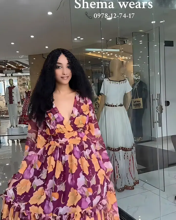 Model in a long plum chiffon dress with a marigold floral print, deep V neckline and tiered skirt