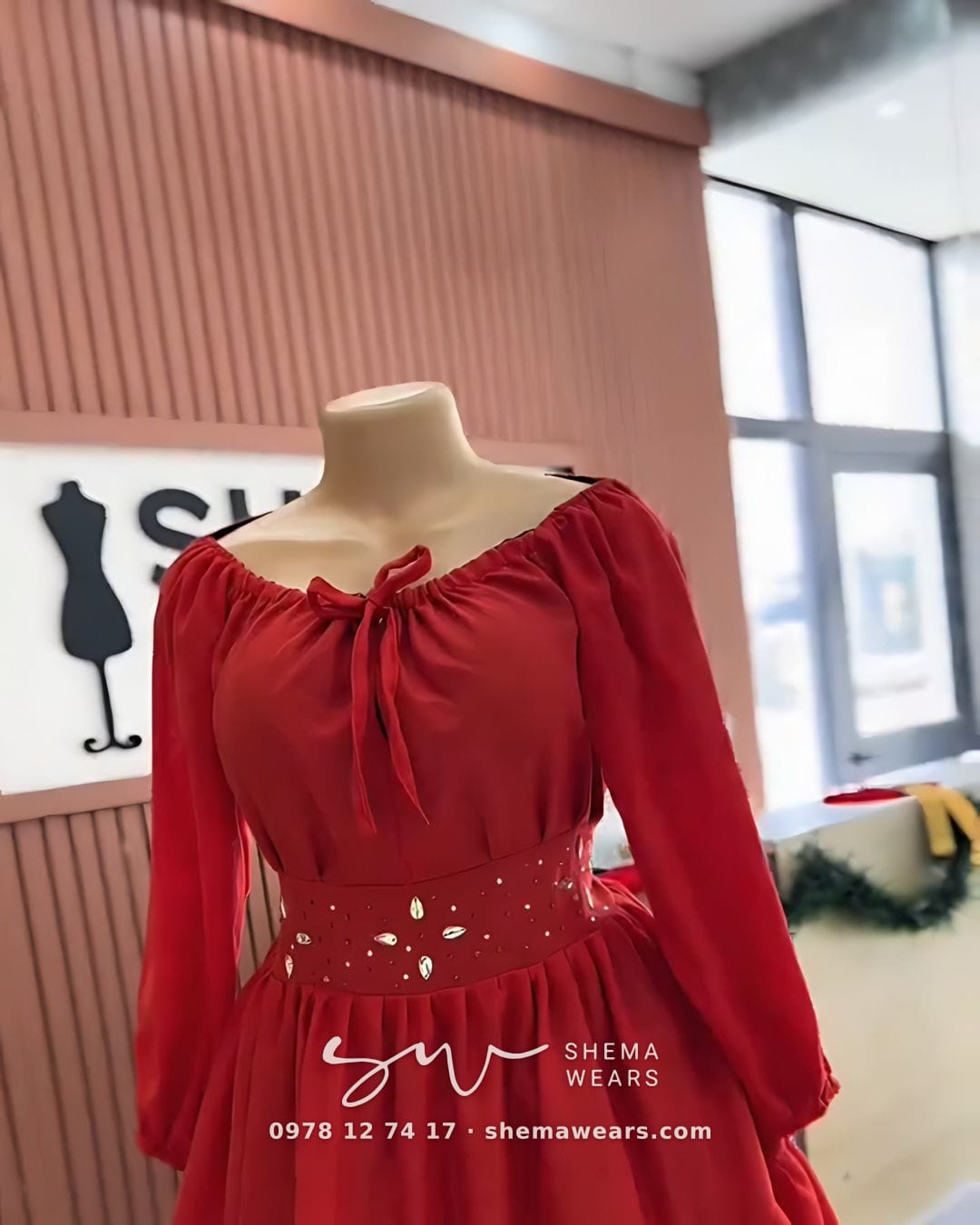 Red long-sleeve dress on a mannequin with a tie neckline, an embellished waistband and a tiered skirt