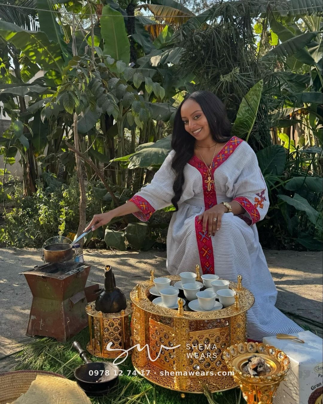 Woman at a coffee ceremony in a loose white kaftan dress with red tibeb at the V neckline, a red cross and red-striped sleeves