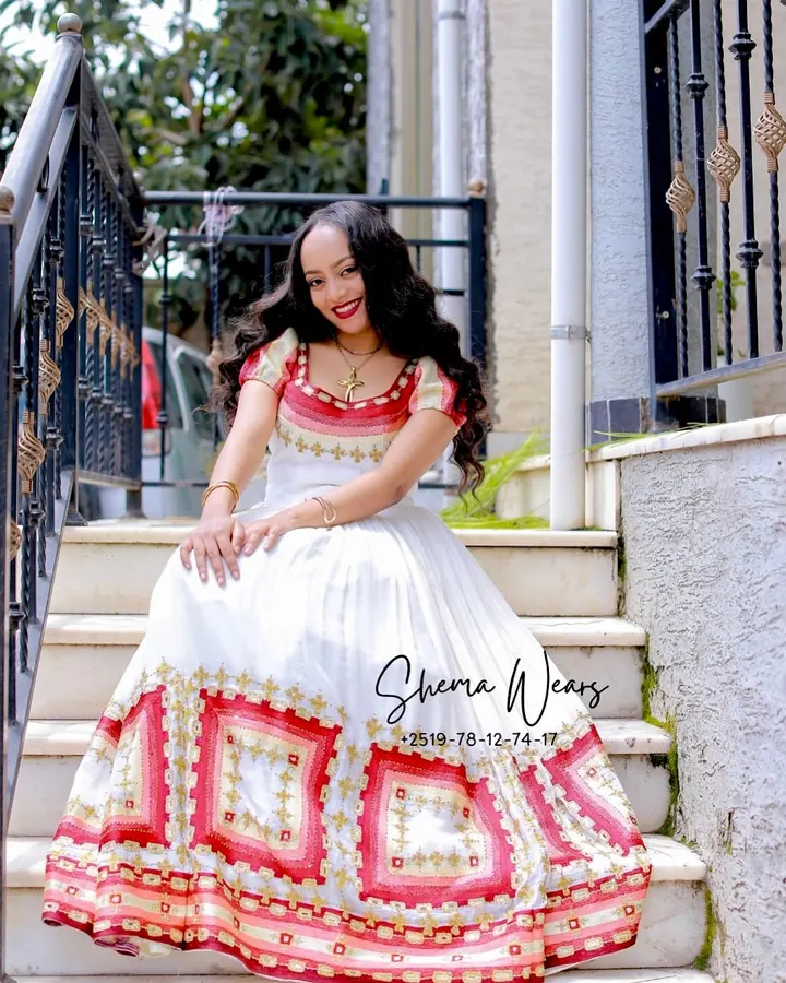 Model sitting on steps in a white habesha kemis with puff sleeves and large red and pink diamond tibeb on the skirt