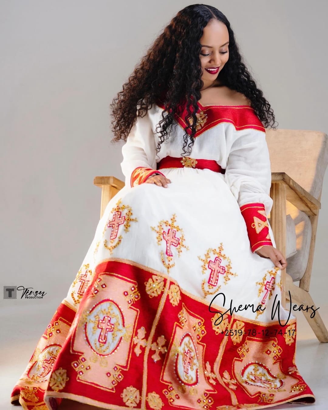 Model in a white habesha kemis with red off-shoulder sleeves, a red belt and large red and gold medallion tibeb on the skirt