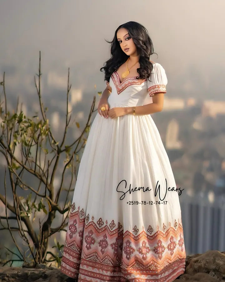 Bride in a white habesha kemis with puff sleeves, rose tibeb at the neckline and a wide rose tibeb hem