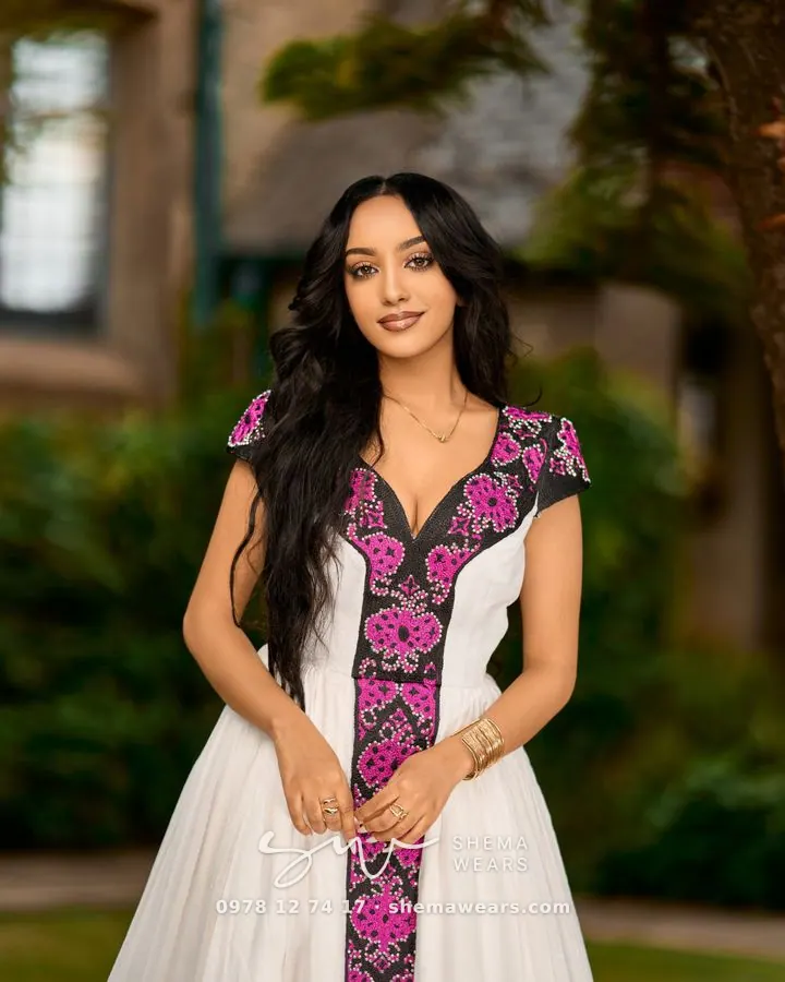 One of the two sisters who founded Shema Wears, in a white habesha kemis with magenta and black tibeb
