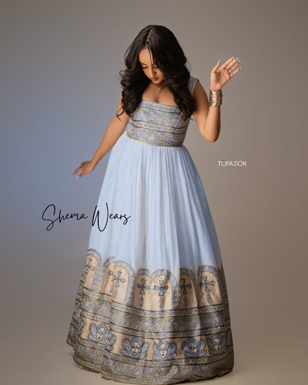 Model in a strapless white habesha gown with silver-grey tibeb on the bodice and a deep hem of crosses