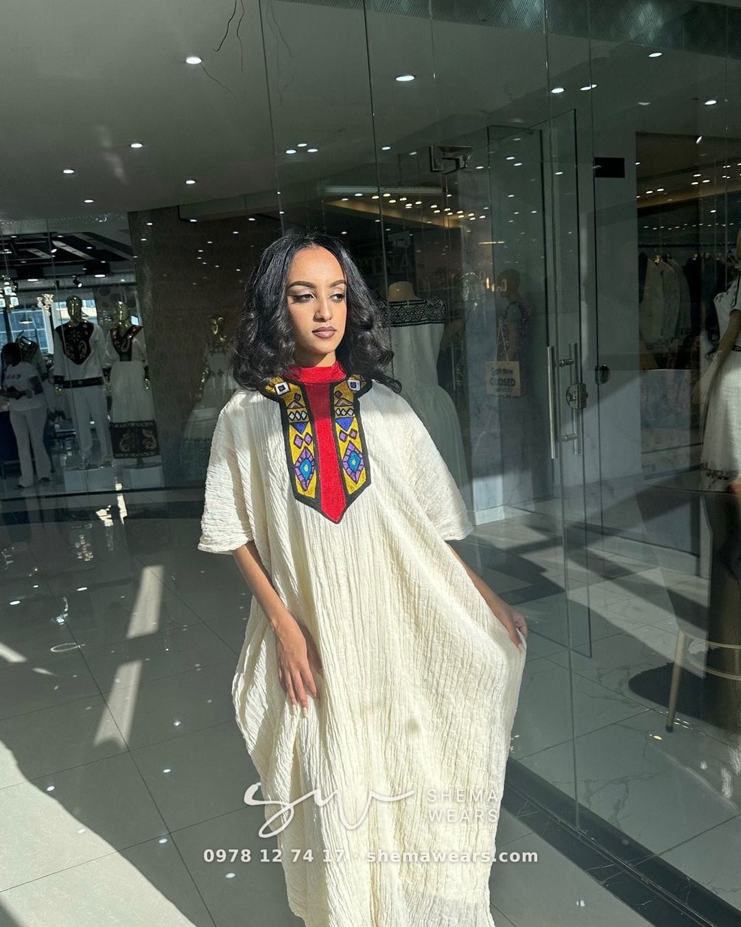 Model in a loose white kaftan-style dress with a red and black tibeb panel at the neckline