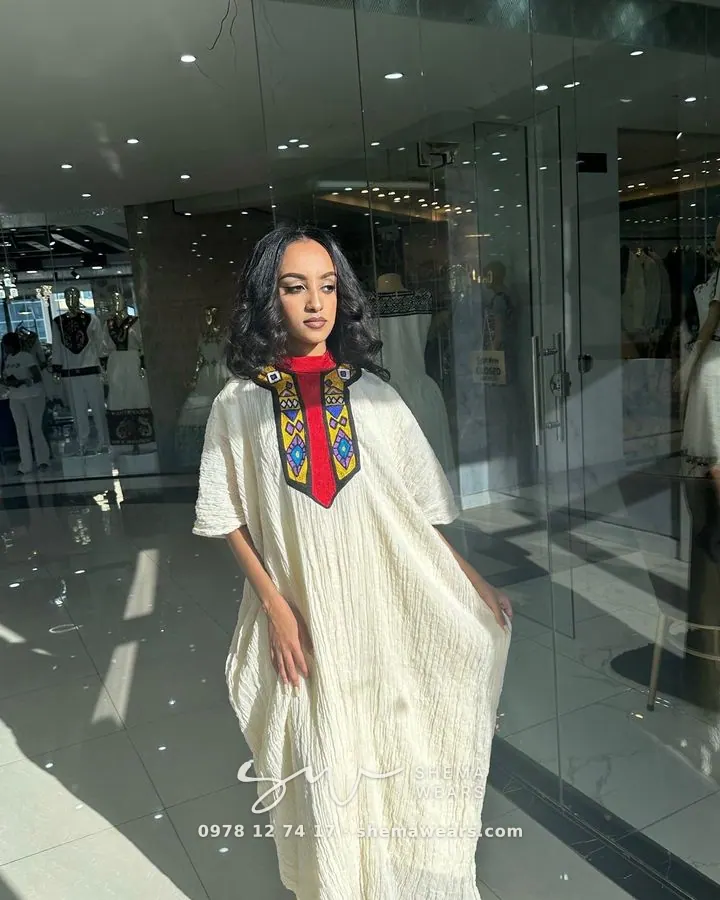 Model in a loose white kaftan-style dress with a red and black tibeb panel at the neckline